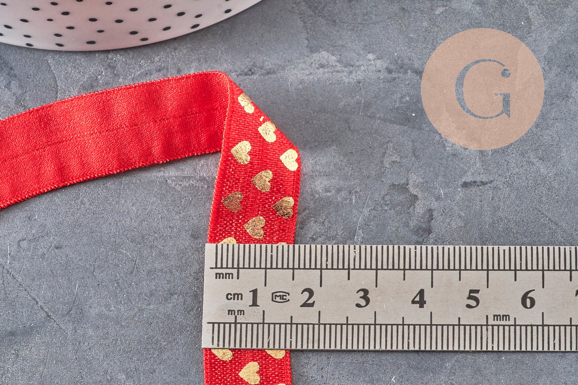 Ruban élastique rouge de 16 mm avec motifs cœurs dorés, mesuré avec une règle sur fond gris.
