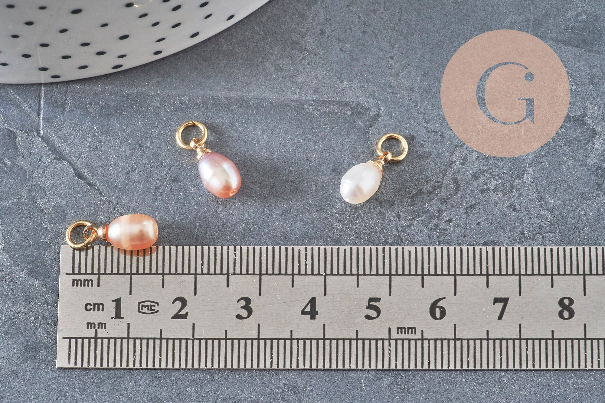 Breloques goutte en perle d'eau douce rose pêche et laiton doré de 11mm sur fond gris avec règle de mesure.