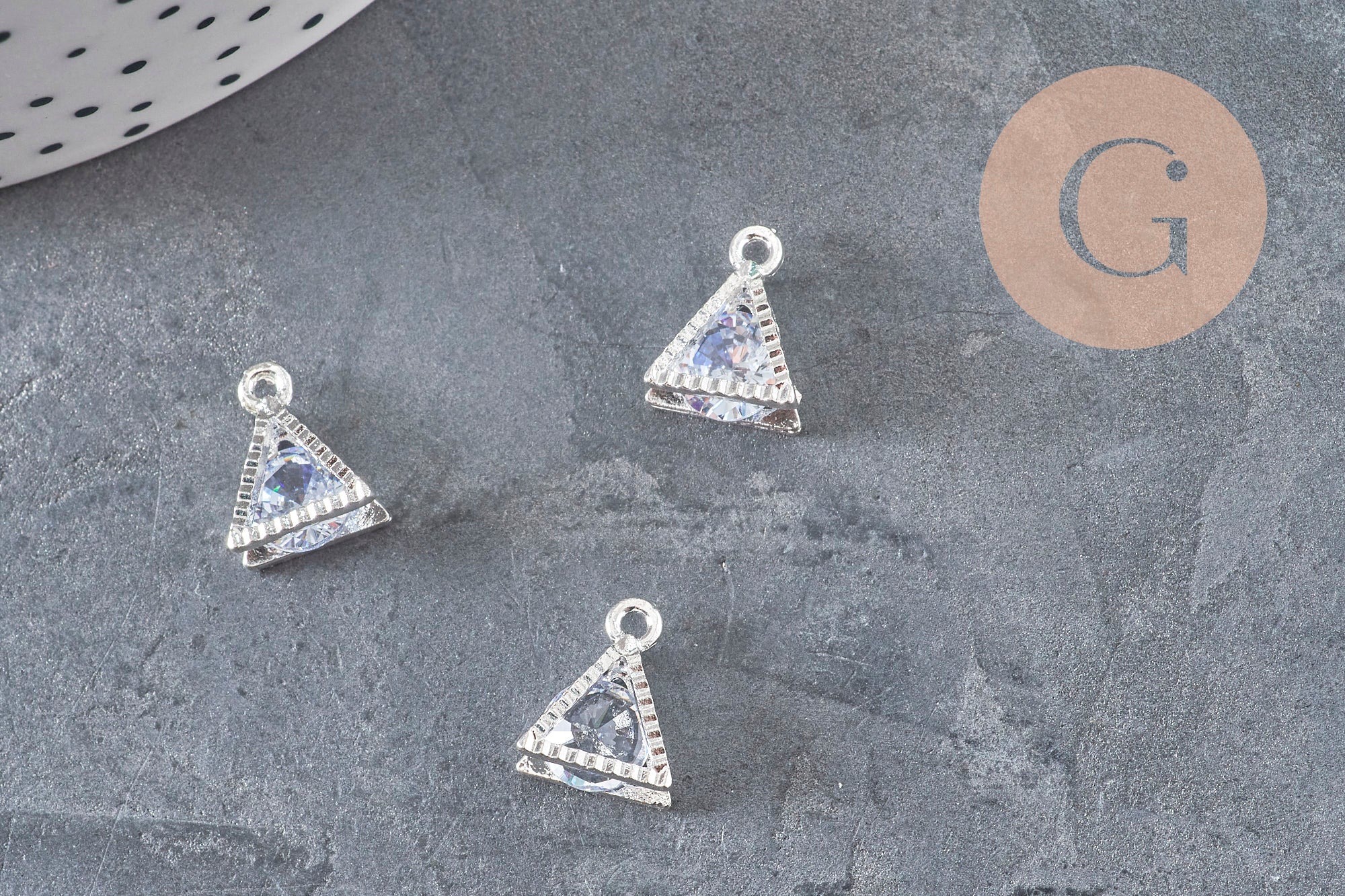 Trois pendentifs triangles 11mm en cristal zircon et zamac argenté sur fond gris.