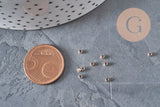 Petites perles à écraser en laiton or rose 2x1.2mm, à côté d'une pièce de 5 centimes.