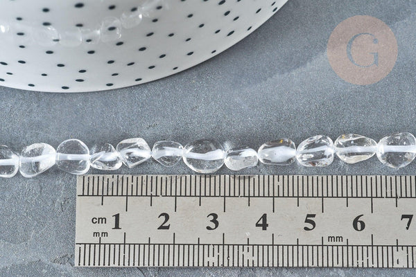 Clear quartz beads, 4–7mm, laid next to a ruler for scale, with a polka-dotted dish edge visible; 40cm strand for jewelry making.