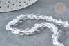 Close-up of Perles cristal de roche roulée, featuring clear, irregular-shaped quartz beads, laid on a gray surface with a dotted white container partially visible.
