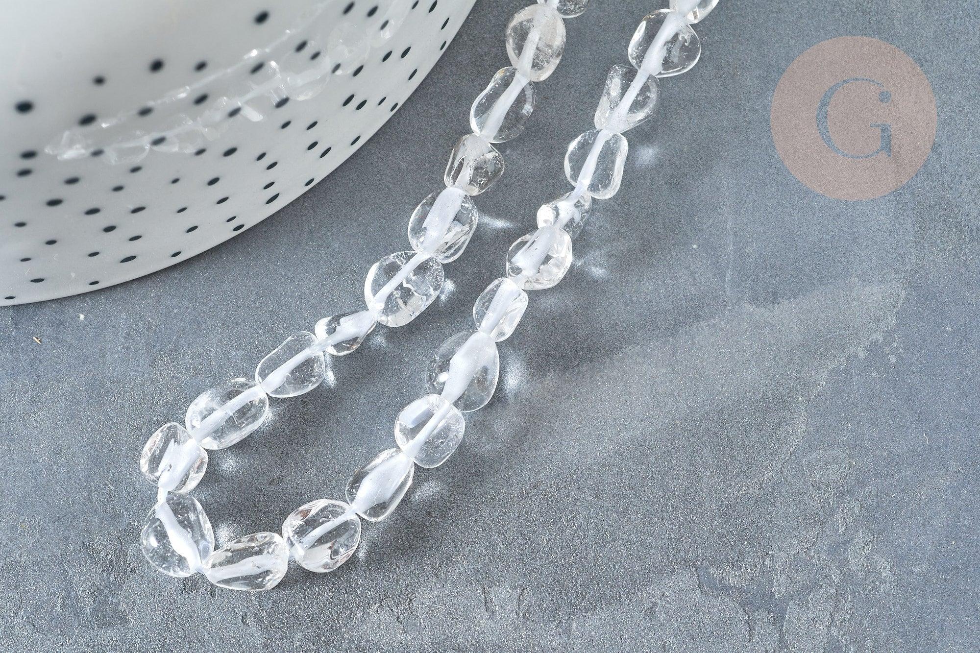 Translucent pebble-shaped glass beads, Perles cristal de roche roulée pierre brute, lie on a dark gray stone surface, beside a dotted white ceramic pot.