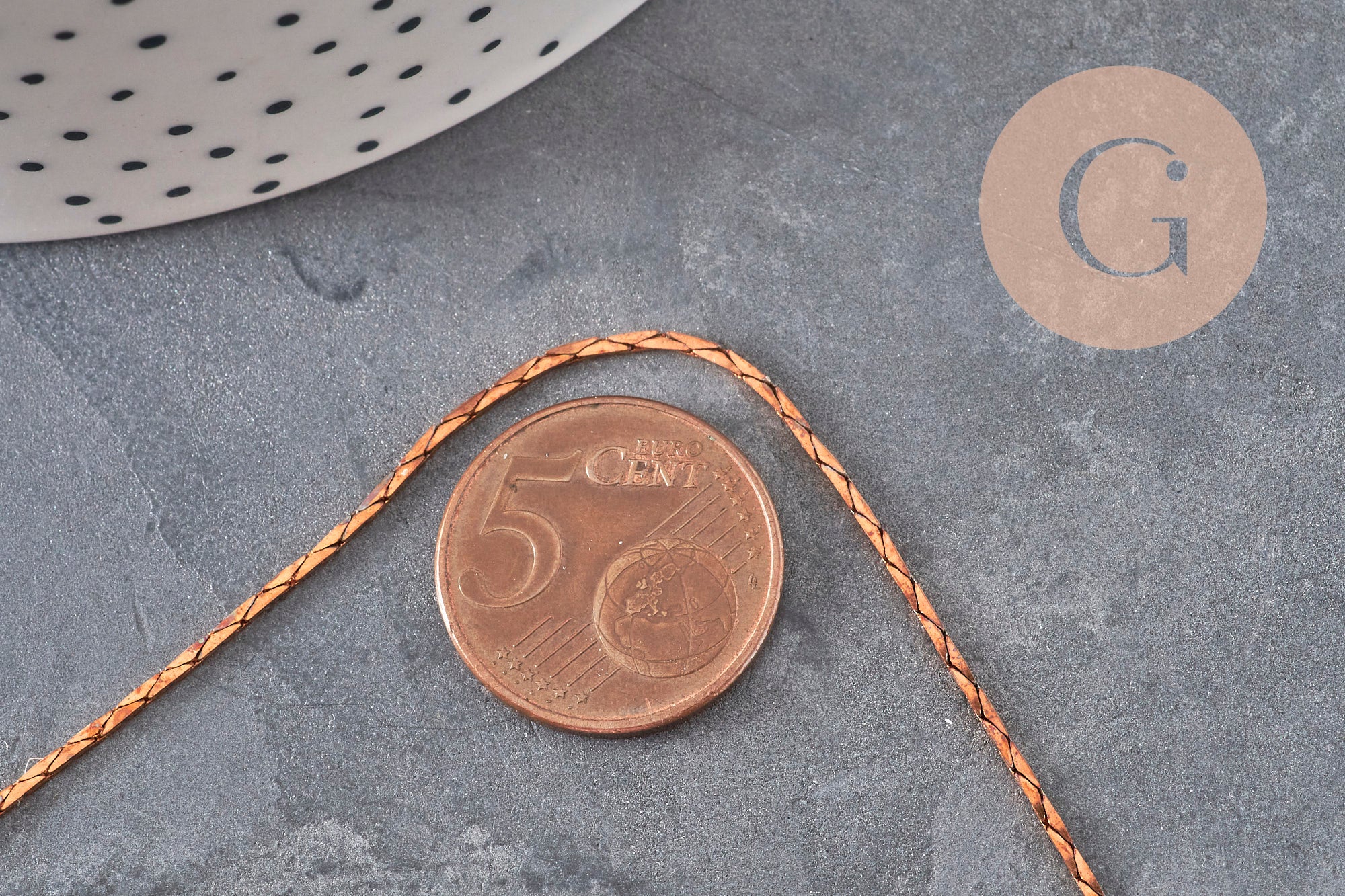 Chaîne forçat fine en laiton brut de 1mm, présentée sur un fond gris avec une pièce de 5 centimes pour l'échelle.