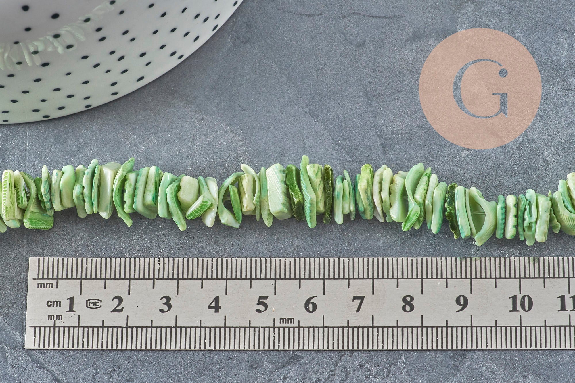 Fil de perles chips coquillage naturel coloré vert clair, 10-20mm, sur fond gris avec règle.