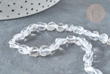 Close-up of Perles cristal de roche roulée, featuring clear, irregular-shaped quartz beads, laid on a gray surface with a dotted white container partially visible.